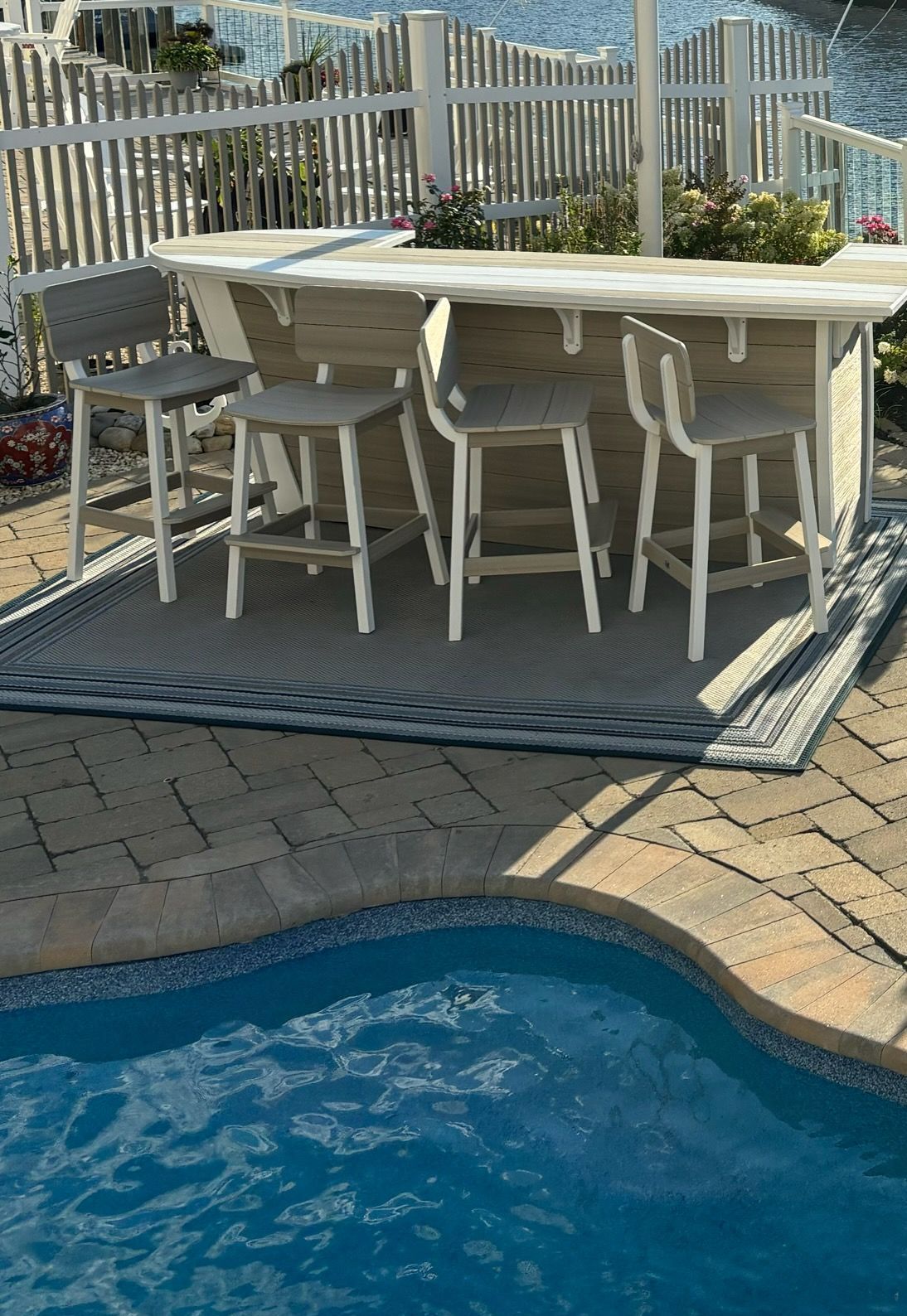 Outdoor bar area with four gray stools, near a pool and a white fence.