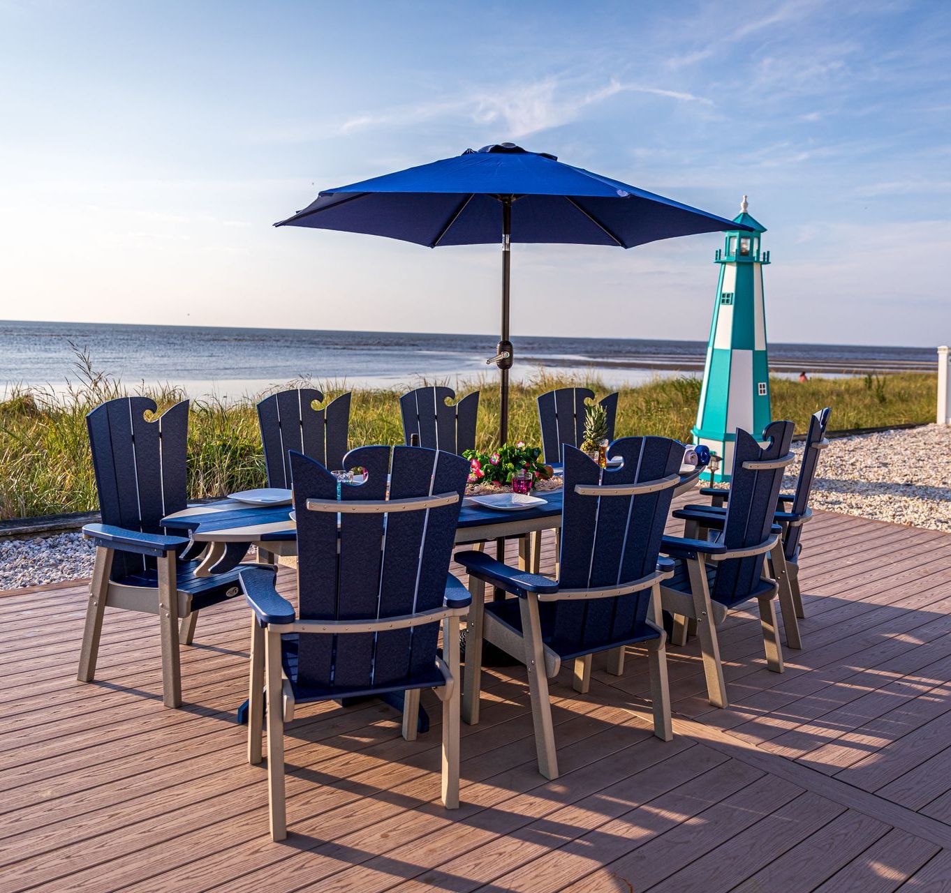 A table with chairs and an umbrella on a deck overlooking the ocean.