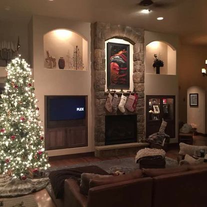 A living room with a christmas tree and stockings on the fireplace.