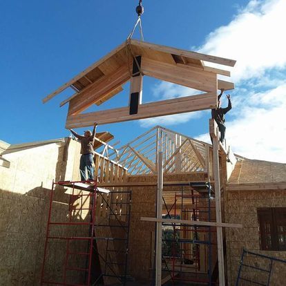 A crane is lifting a piece of wood over a house under construction