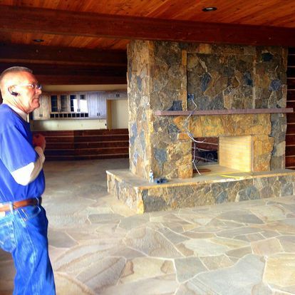 A man in a blue shirt stands in front of a stone fireplace