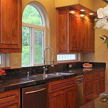 A kitchen with wooden cabinets , a sink , a dishwasher , and a window.