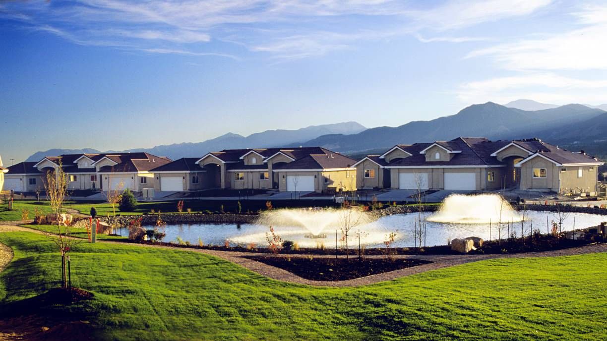 A row of houses with a pond in front of them and mountains in the background.