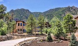 A house in the middle of a forest with mountains in the background.