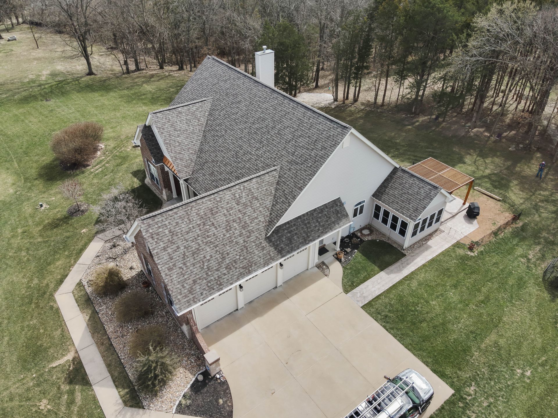 Aerial view of a house with a gray roof, white siding, and a concrete driveway.