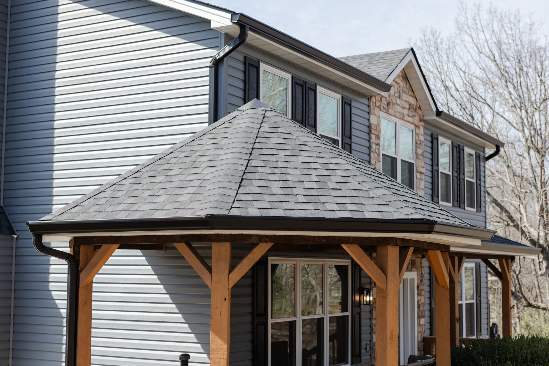 Blue house with brown wooden porch and gray shingle roof.