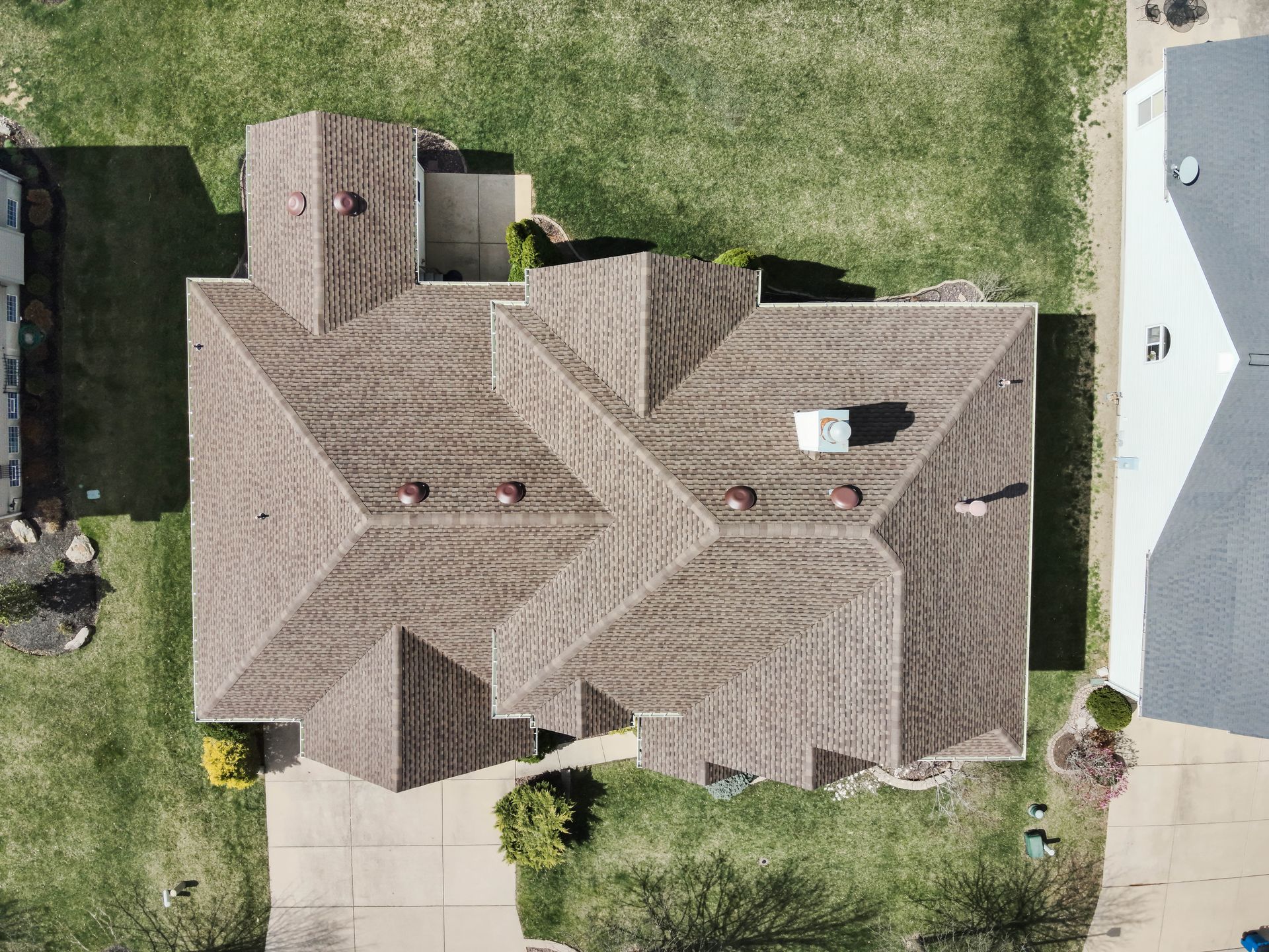 Overhead view of a house with a brown roof, green lawn, and a driveway.