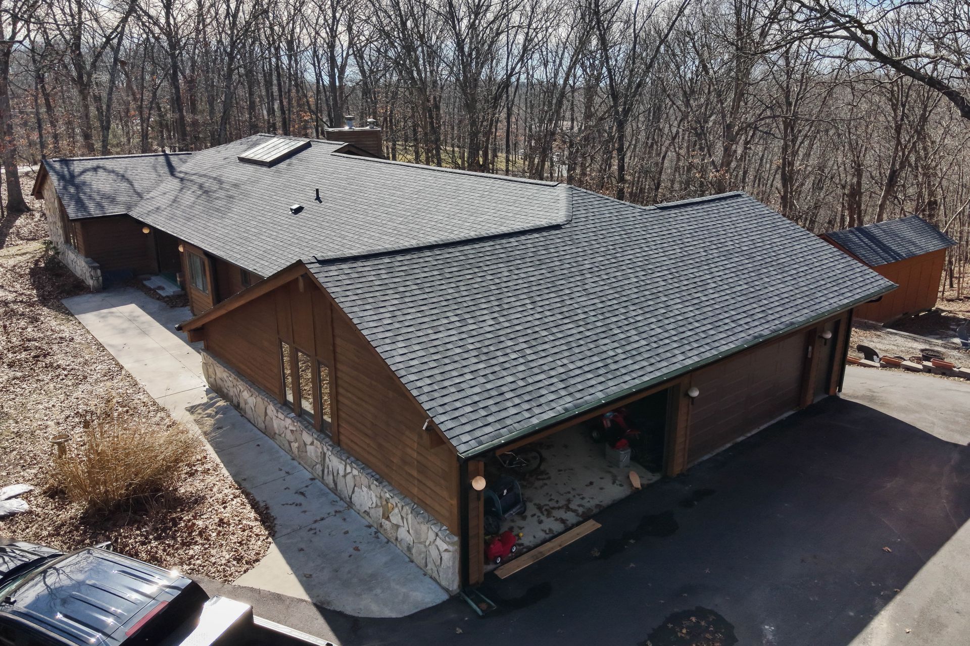Brown house with gray roof and a two-car garage in a wooded area.