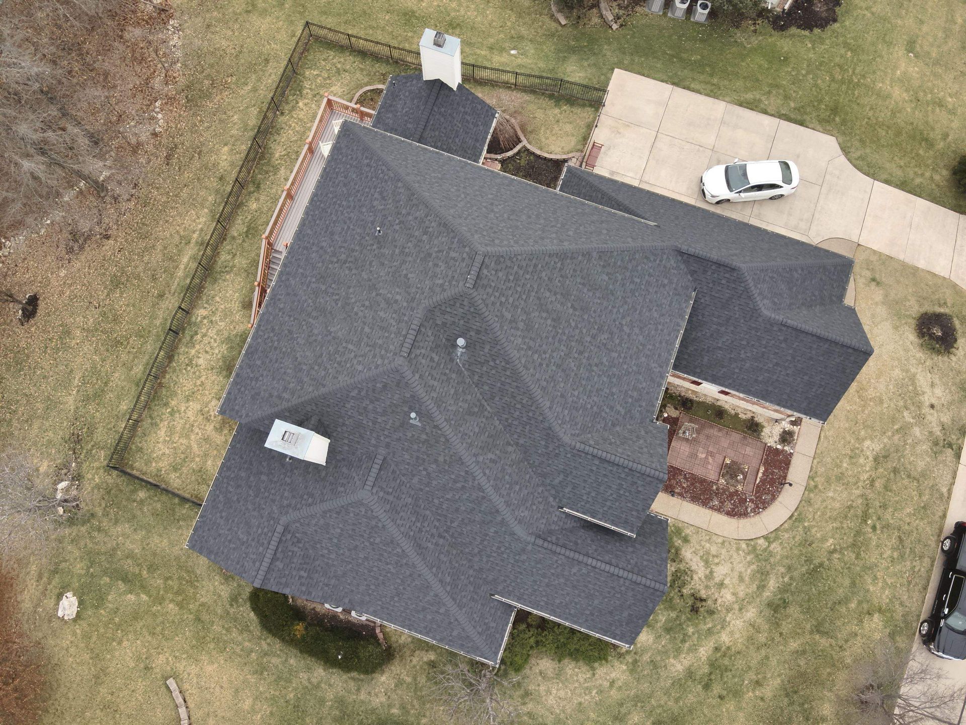Aerial view of a house with a dark gray roof, chimney, and a car in the driveway.