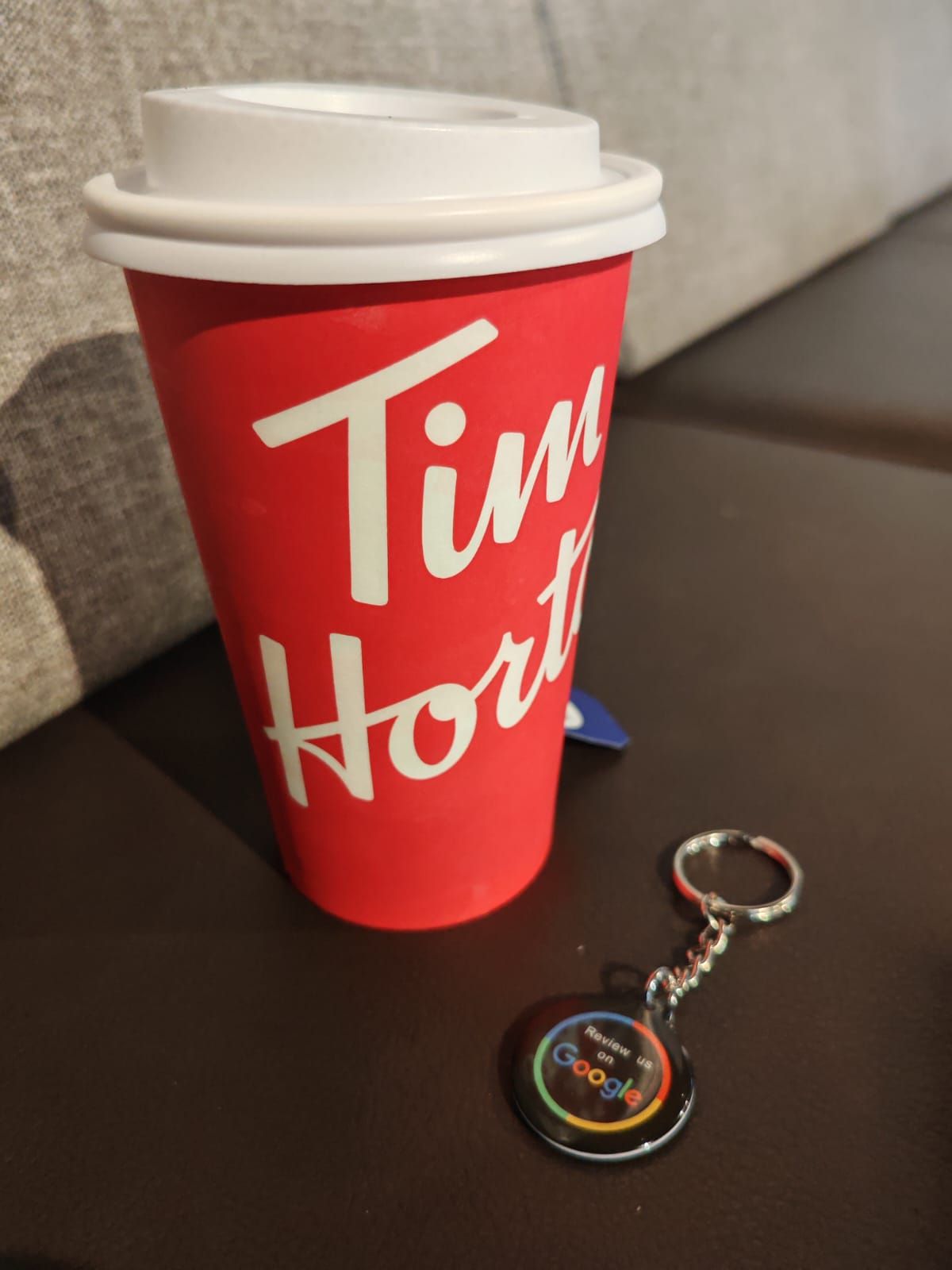 Red Tim Hortons travel mug and Google keychain on a dark surface.