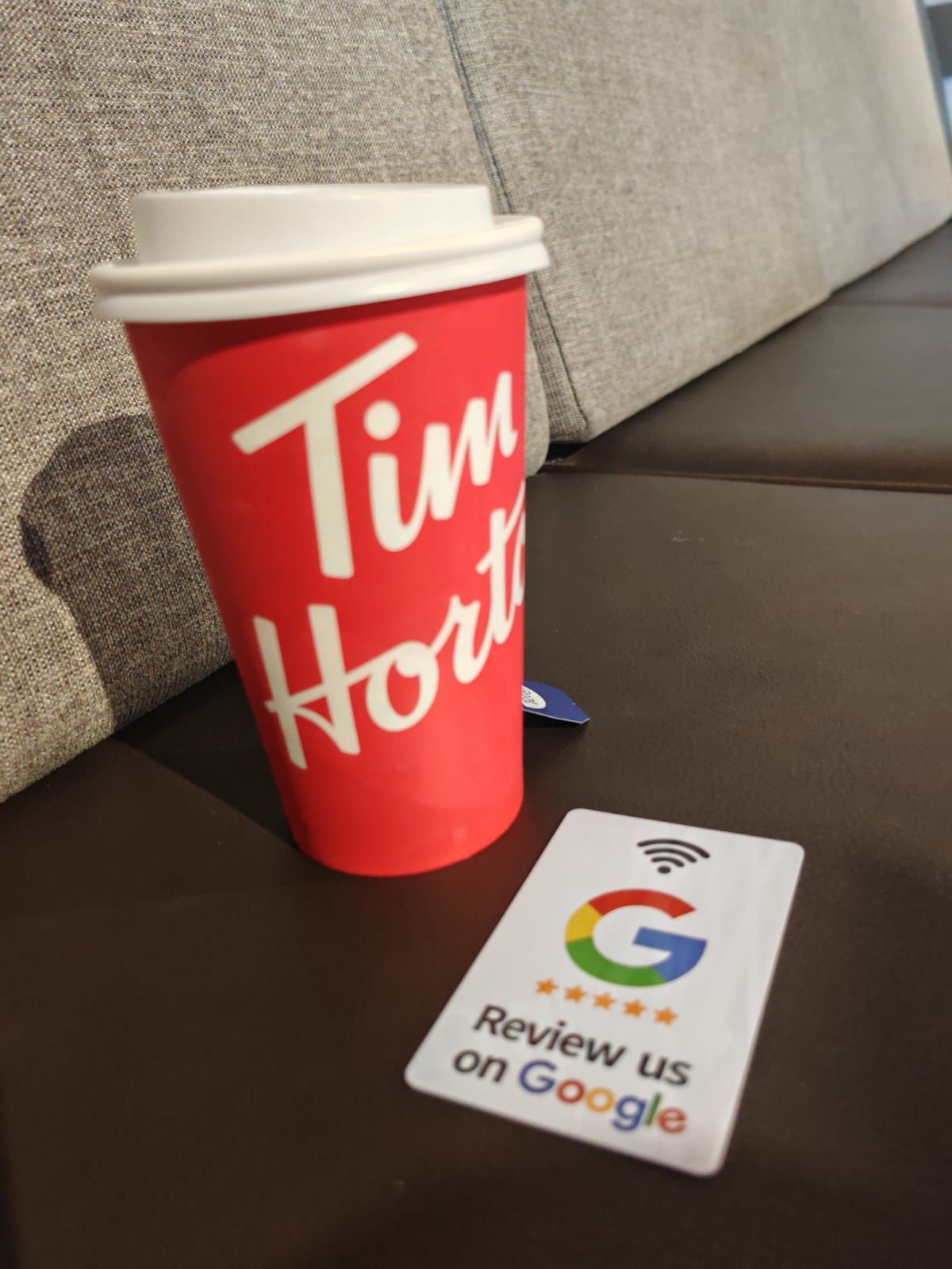Red Tim Hortons coffee cup and Google review card on a dark surface.