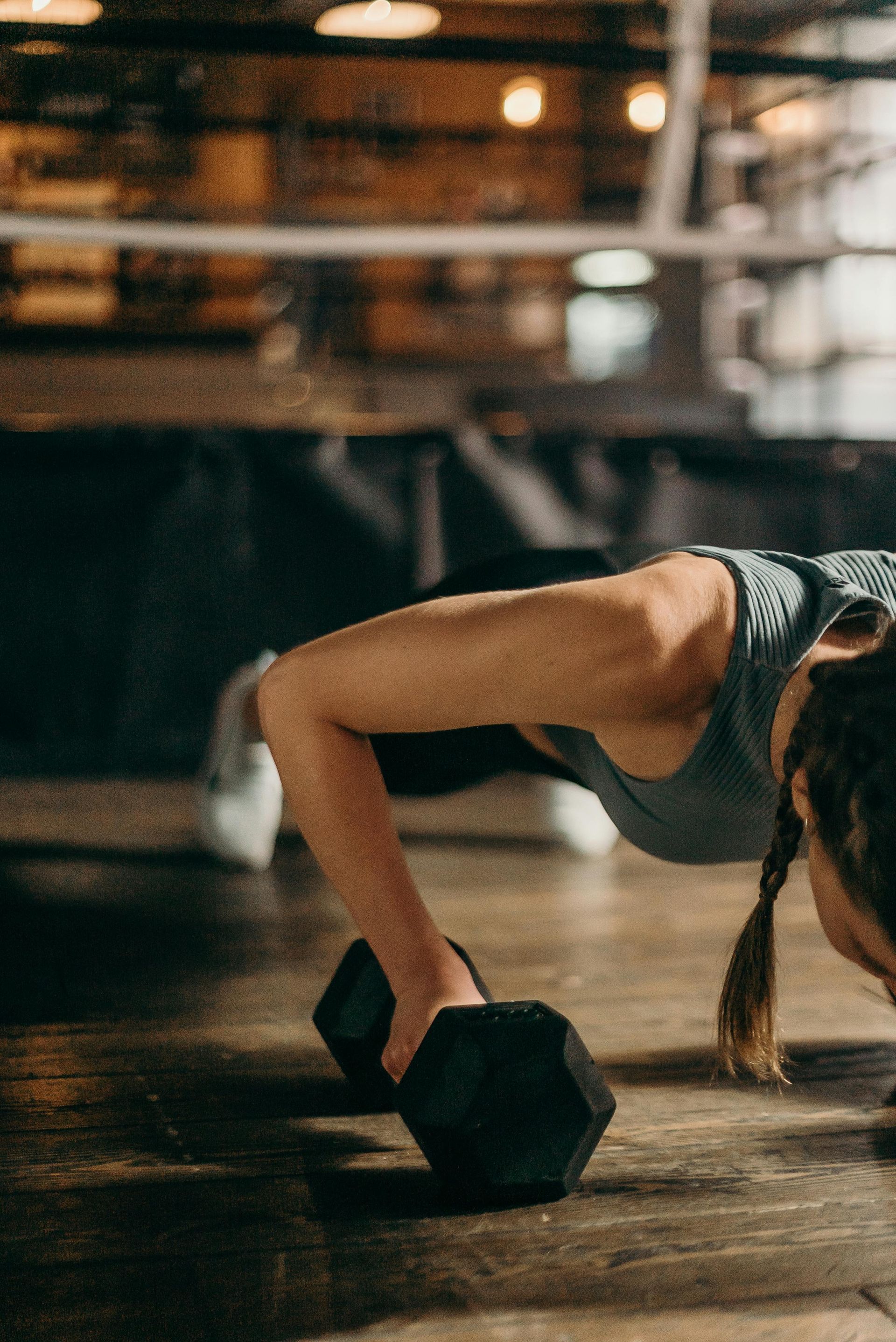 Woman doing push-ups with hands on dumbbells in a gym.