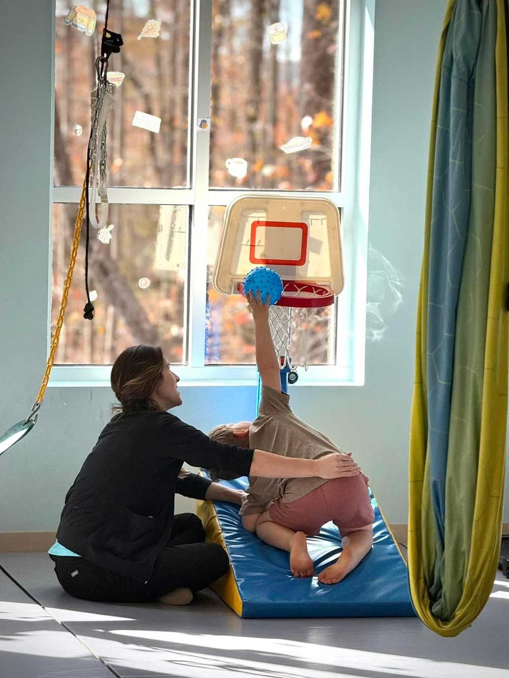 A woman is helping a child with a basketball hoop in a gym.