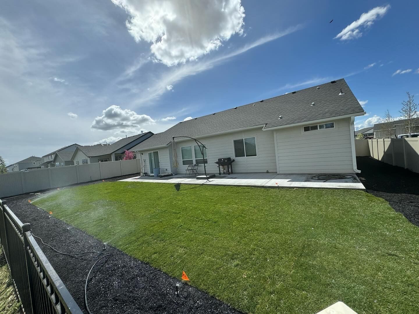 A sprinkler is spraying water on a lush green lawn in front of a house.
