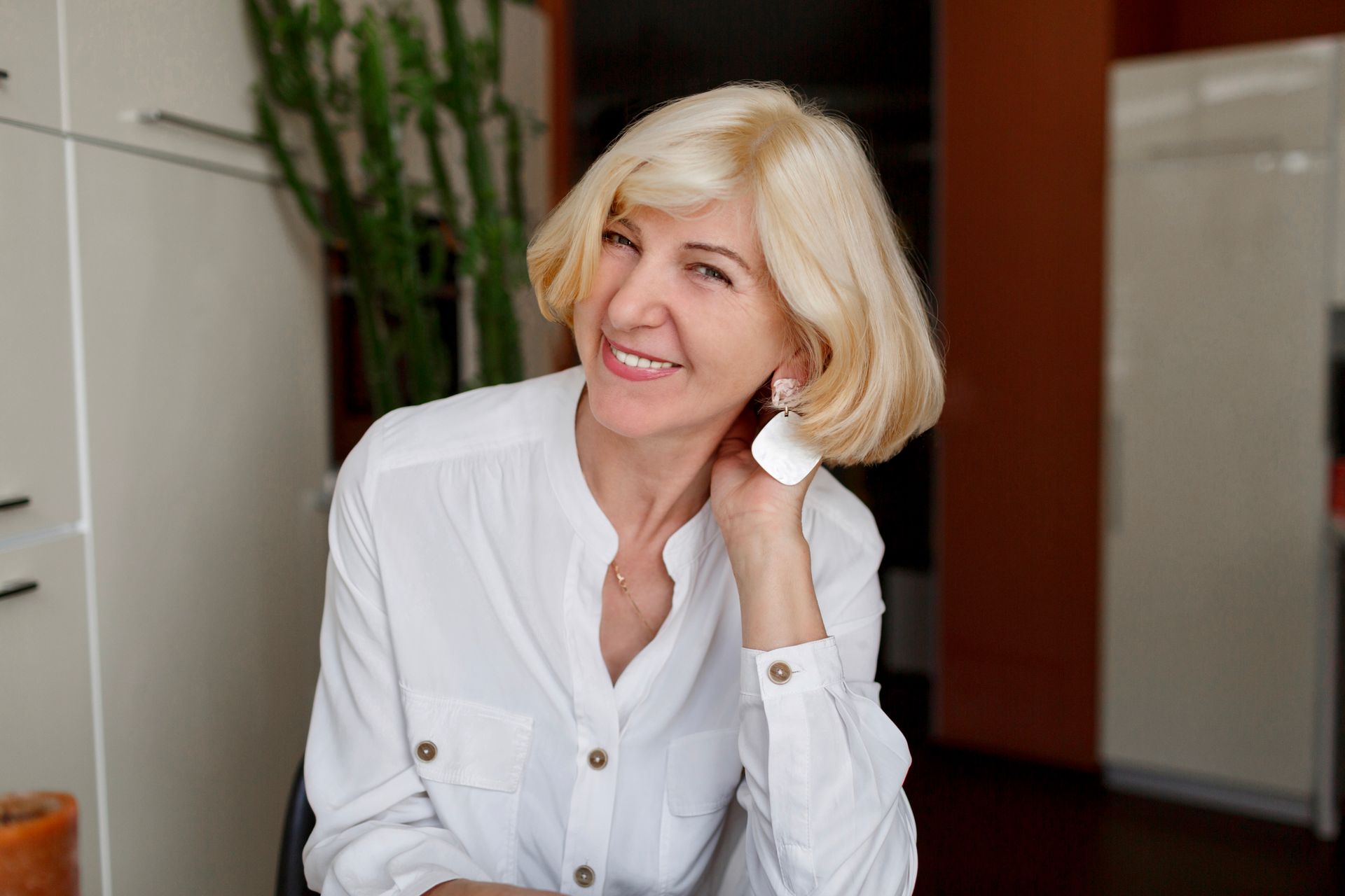 An elderly woman in a white shirt is smiling while sitting at a table.