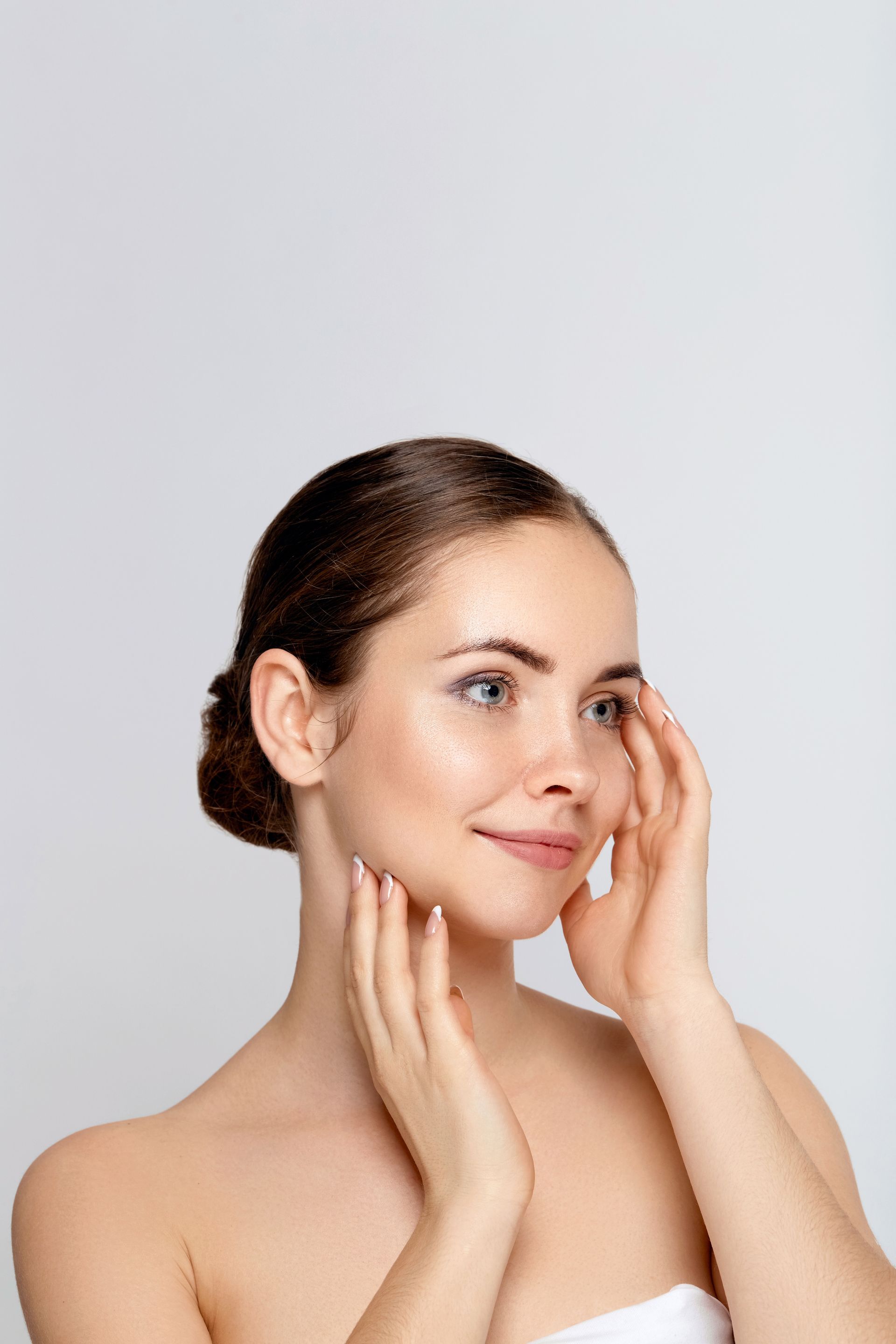 A woman is touching her face with her hands and smiling.