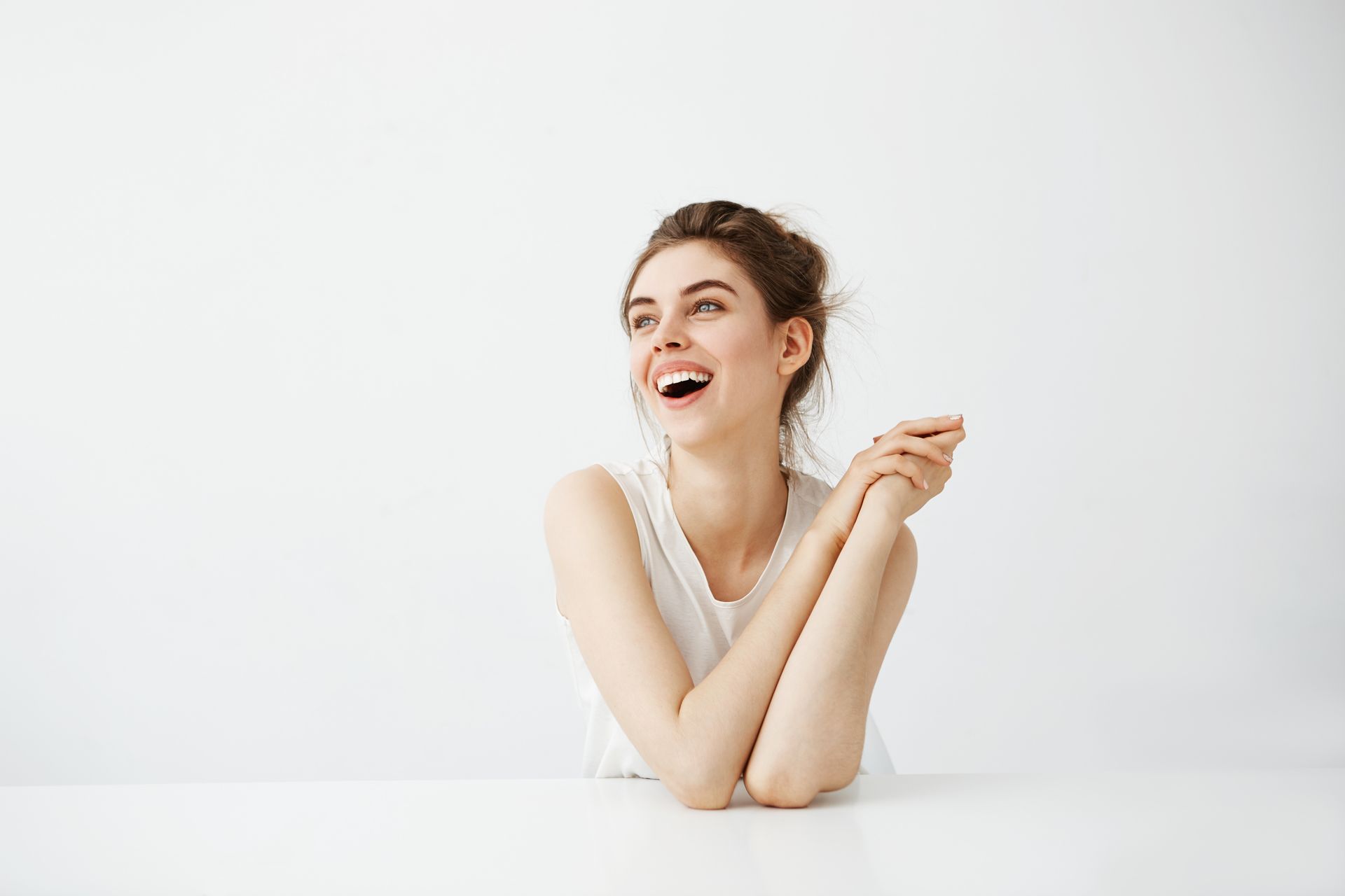 A woman is sitting at a table with her arms crossed and smiling.
