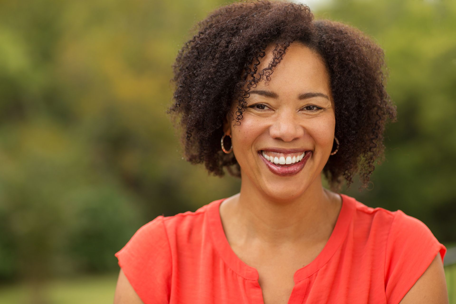 A woman in a red shirt is smiling for the camera.