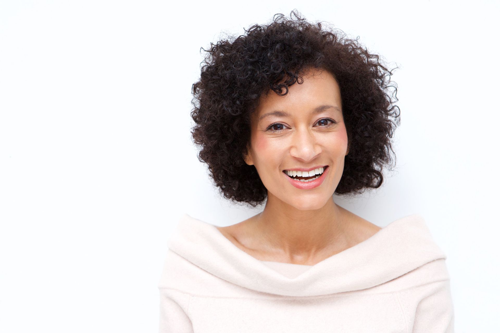 A woman with curly hair is smiling and wearing a white sweater.