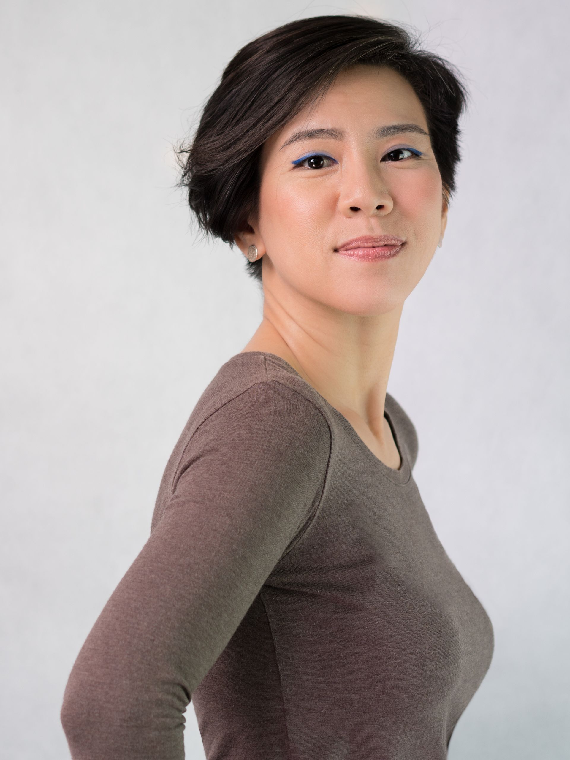 A woman with short hair is wearing a brown shirt and looking at the camera.