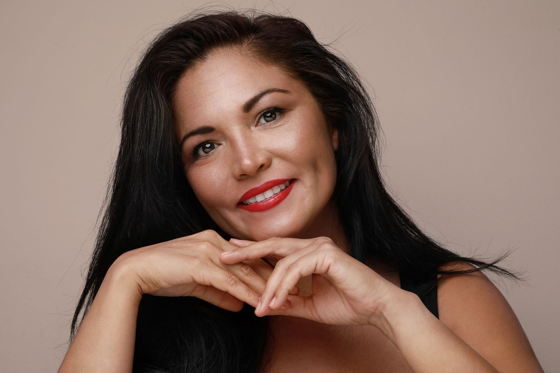 A woman with long black hair and red lipstick is smiling.