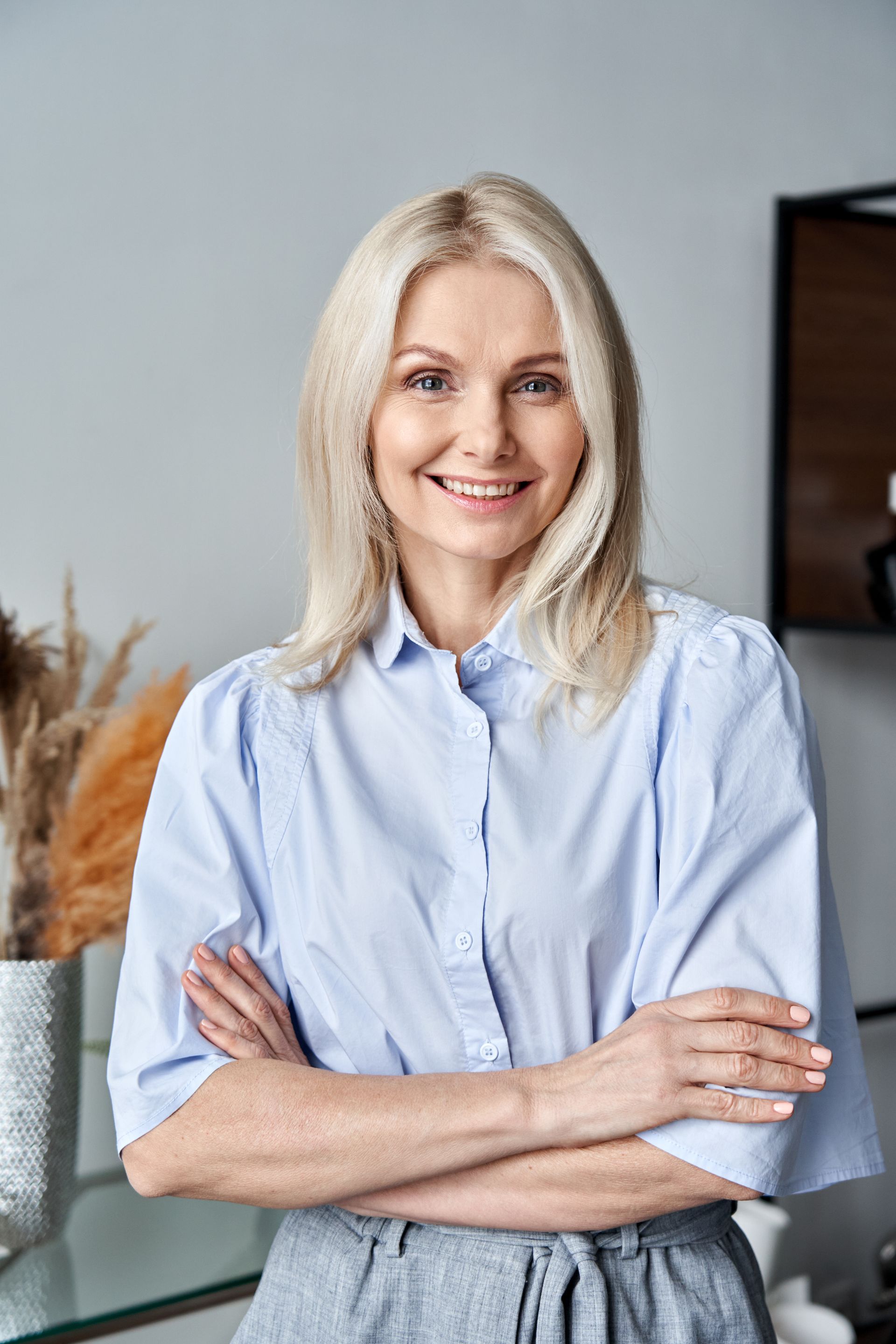 A woman in a blue shirt is standing with her arms crossed and smiling.