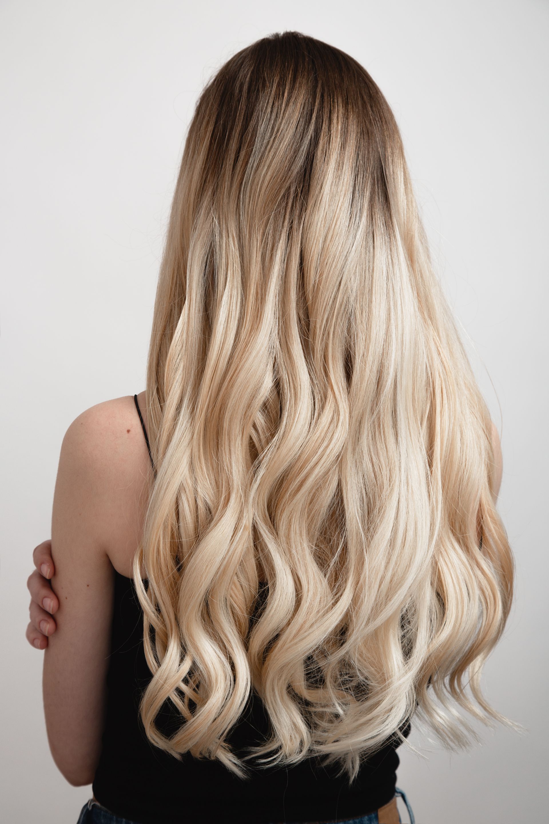 A woman with long blonde hair is wearing a black tank top and jeans.