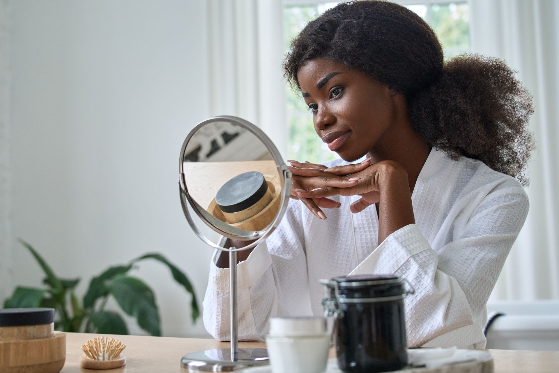 A woman is looking at her face in a mirror.