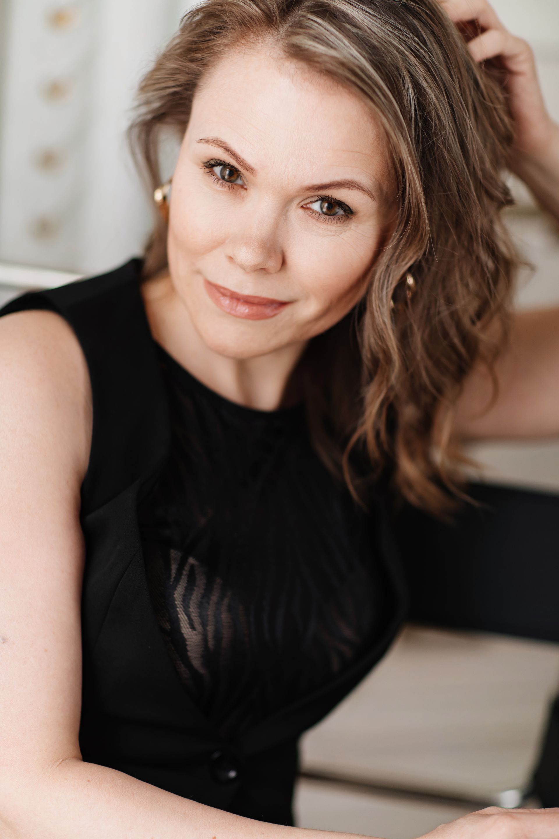 A woman in a black dress is sitting in a chair and touching her hair.