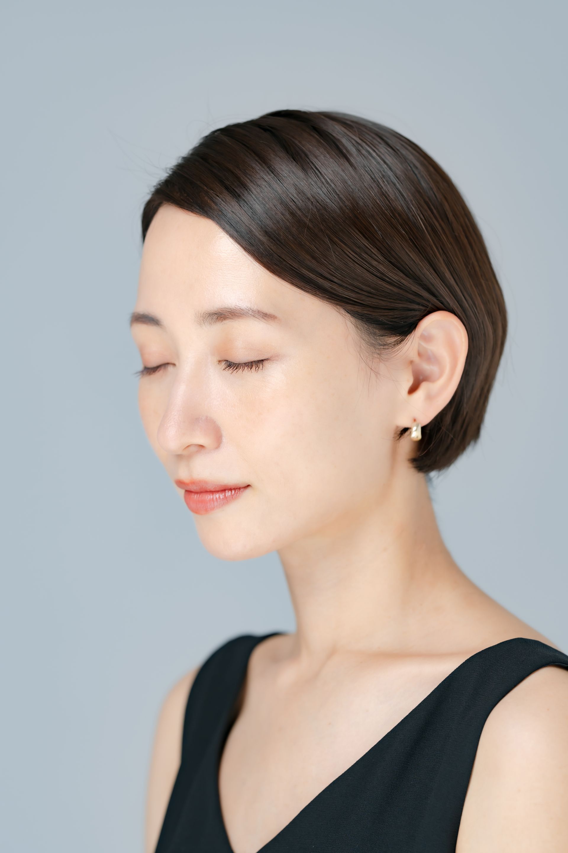 A woman wearing a black dress and earrings is looking down with her eyes closed.