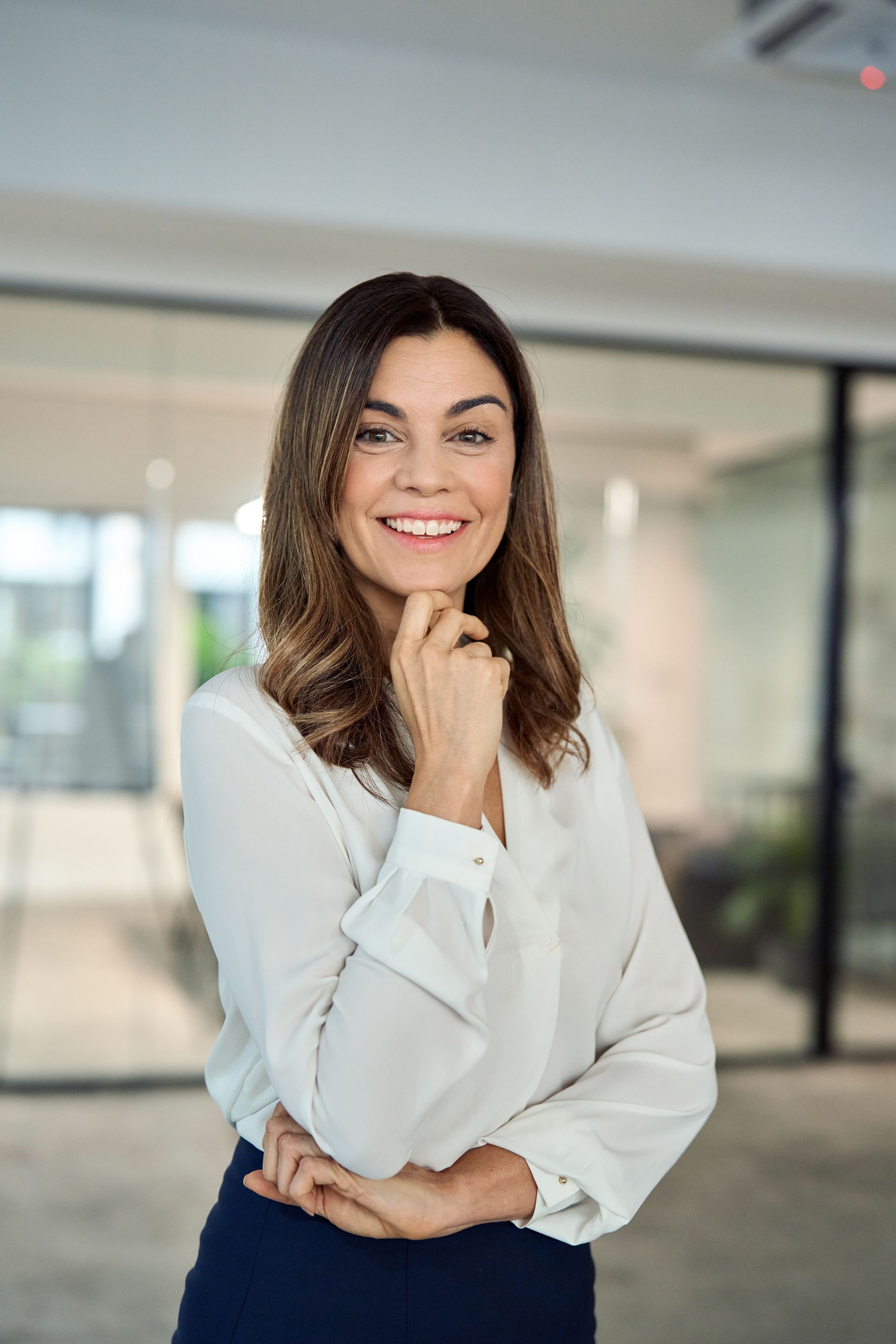 A woman in a white shirt is smiling with her hand on her chin.
