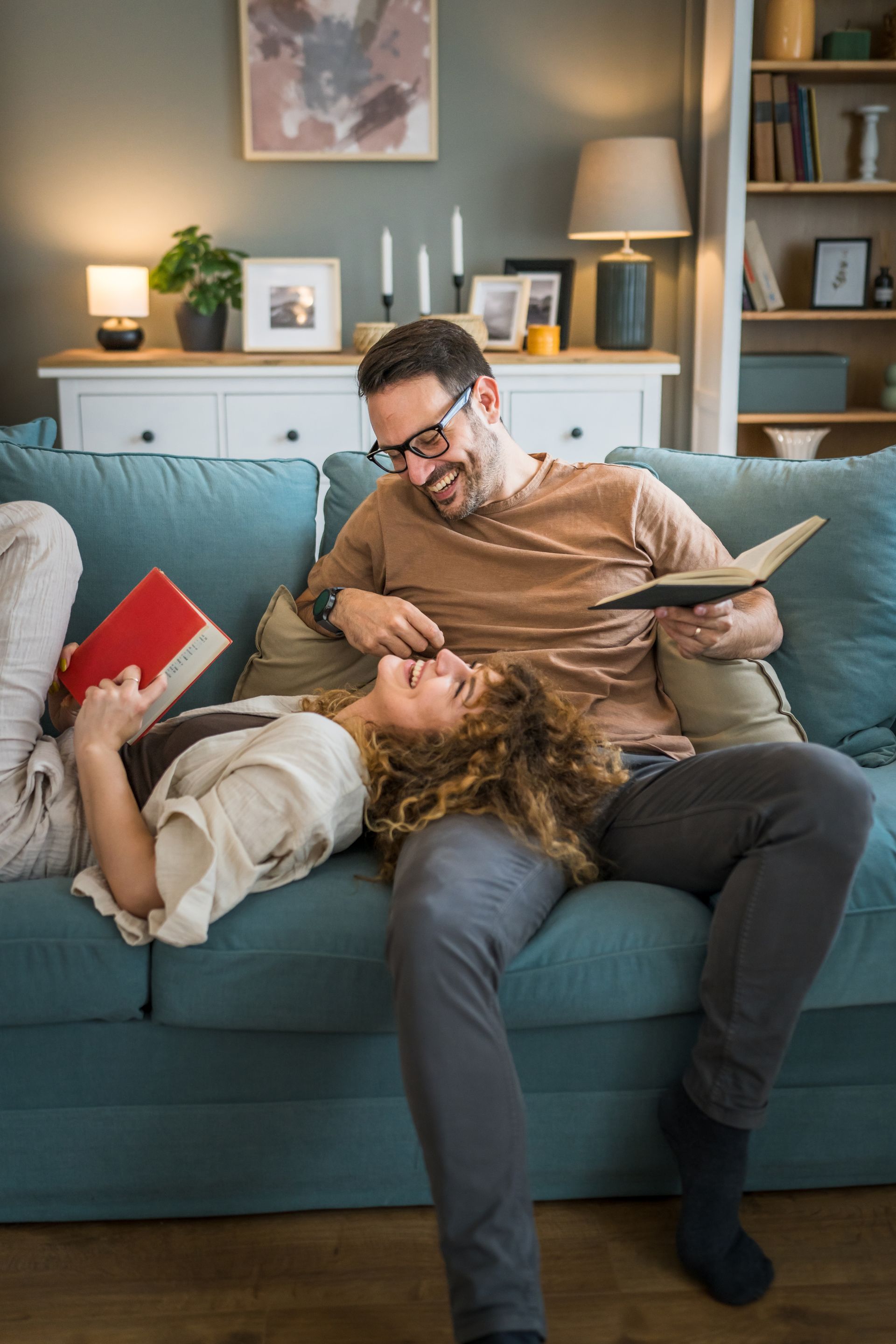 A man and a woman are sitting on a couch reading books.