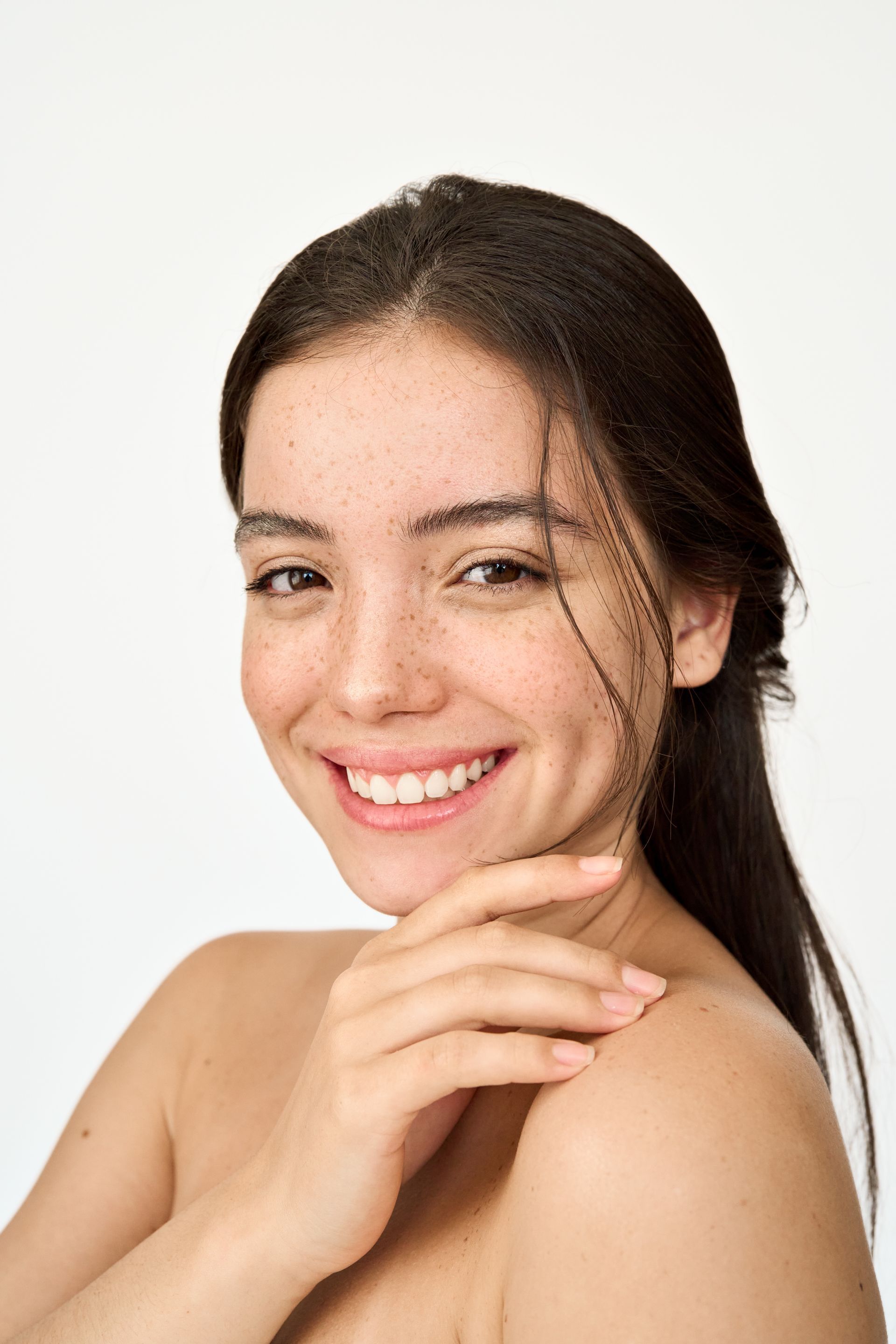 A woman without a shirt is smiling and touching her face.
