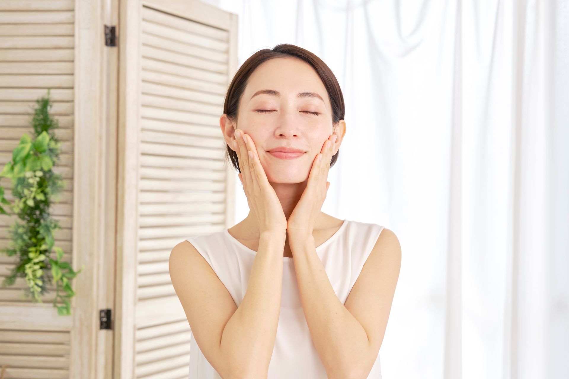 A woman is touching her face with her hands and smiling.