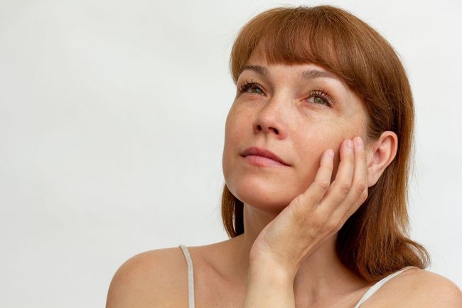 A woman is holding her hand to her face and looking up.