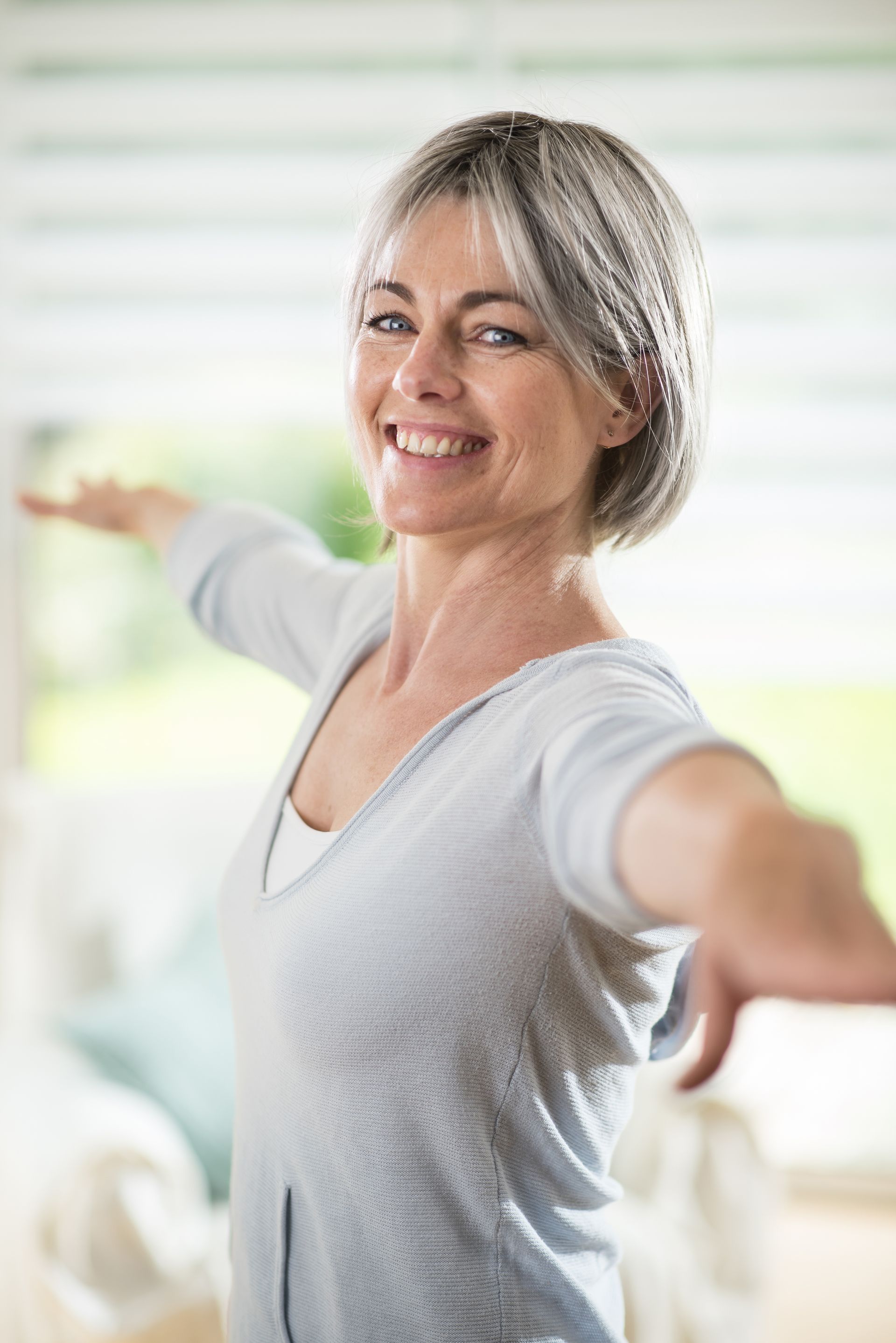 A woman is smiling and stretching her arms in a living room.
