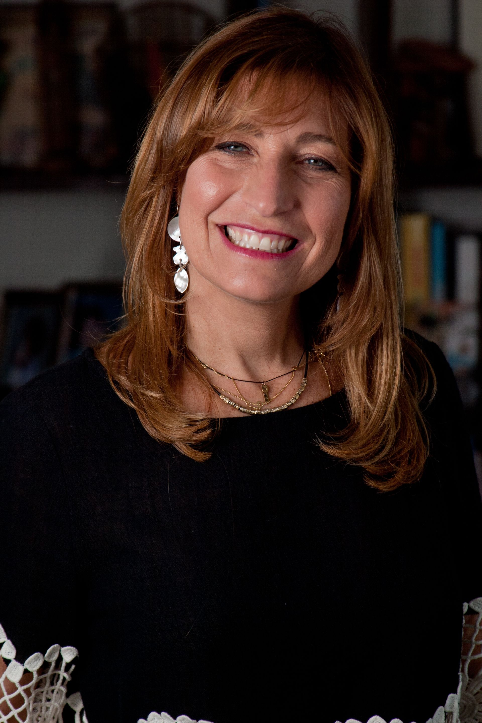 A woman wearing a black dress and earrings is smiling for the camera.