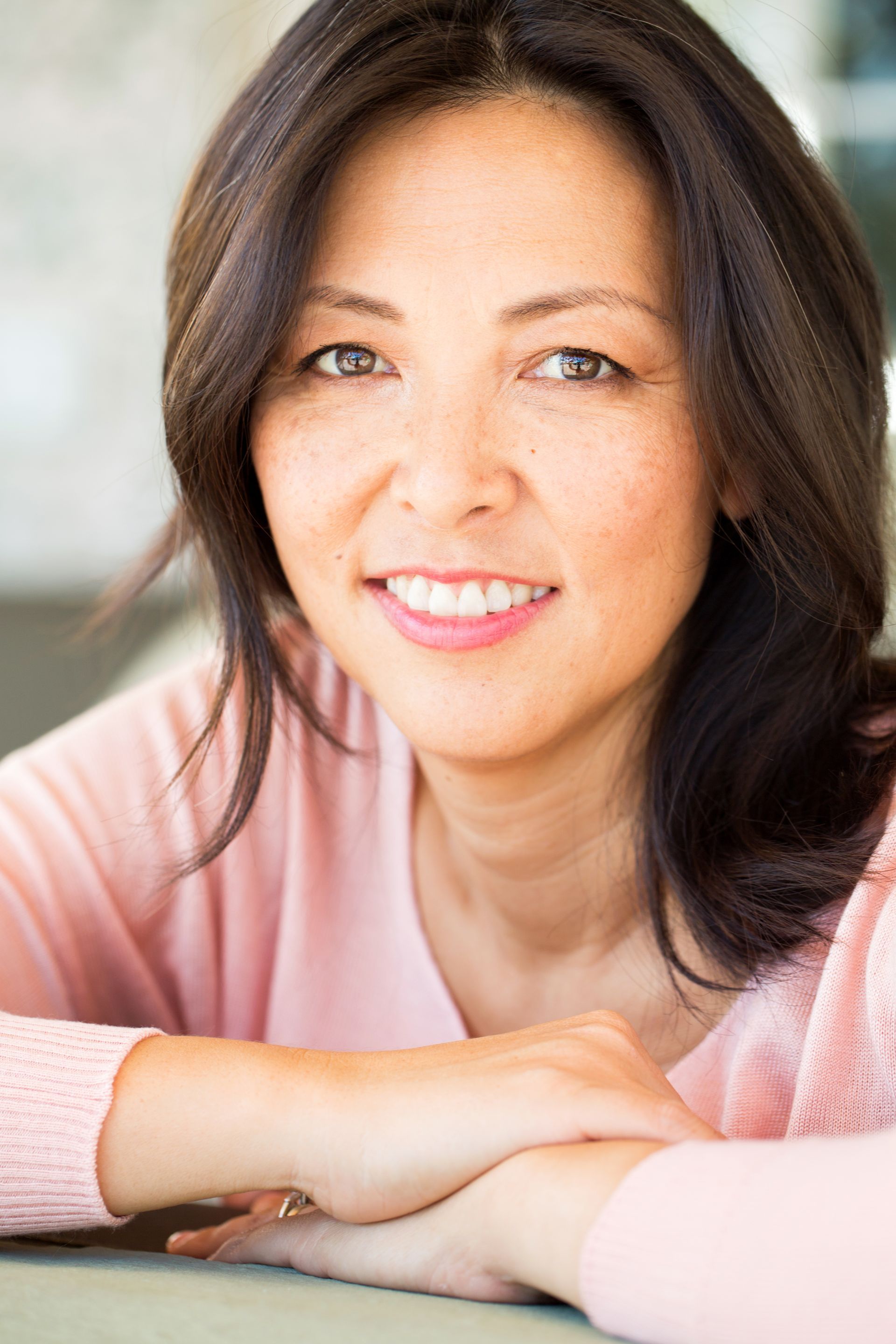 A woman in a pink sweater is smiling with her hands on her hips.
