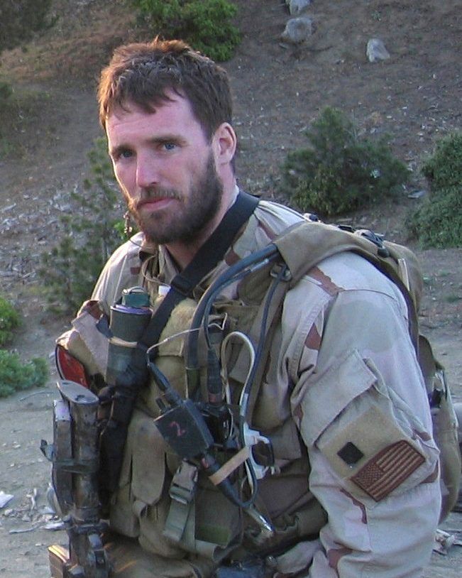 A man with a beard is wearing a military uniform and a backpack.