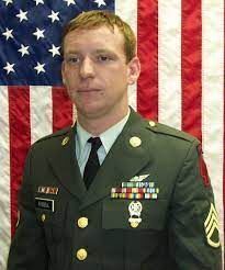 A man in a military uniform and tie is standing in front of an american flag.