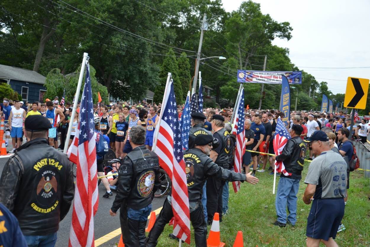 A group of people holding american flags are standing on the side of the road.