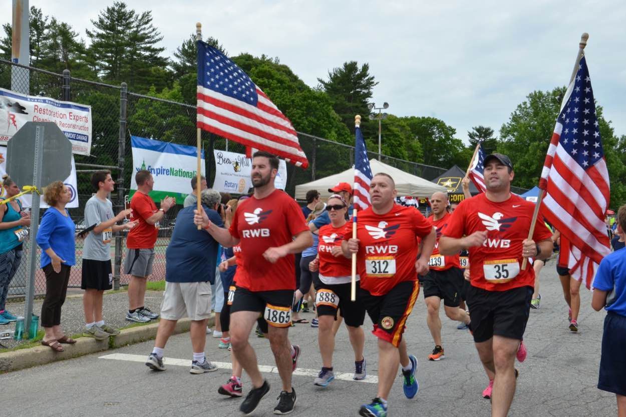 A group of people are running down a street holding american flags.