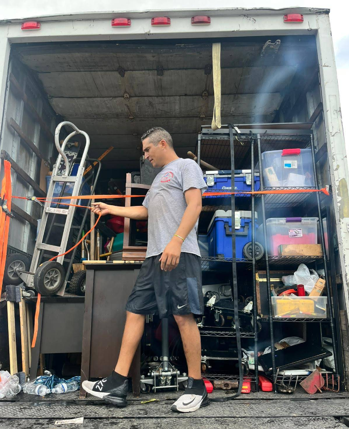 Man standing in the back of a moving truck pointing at packed shelving.