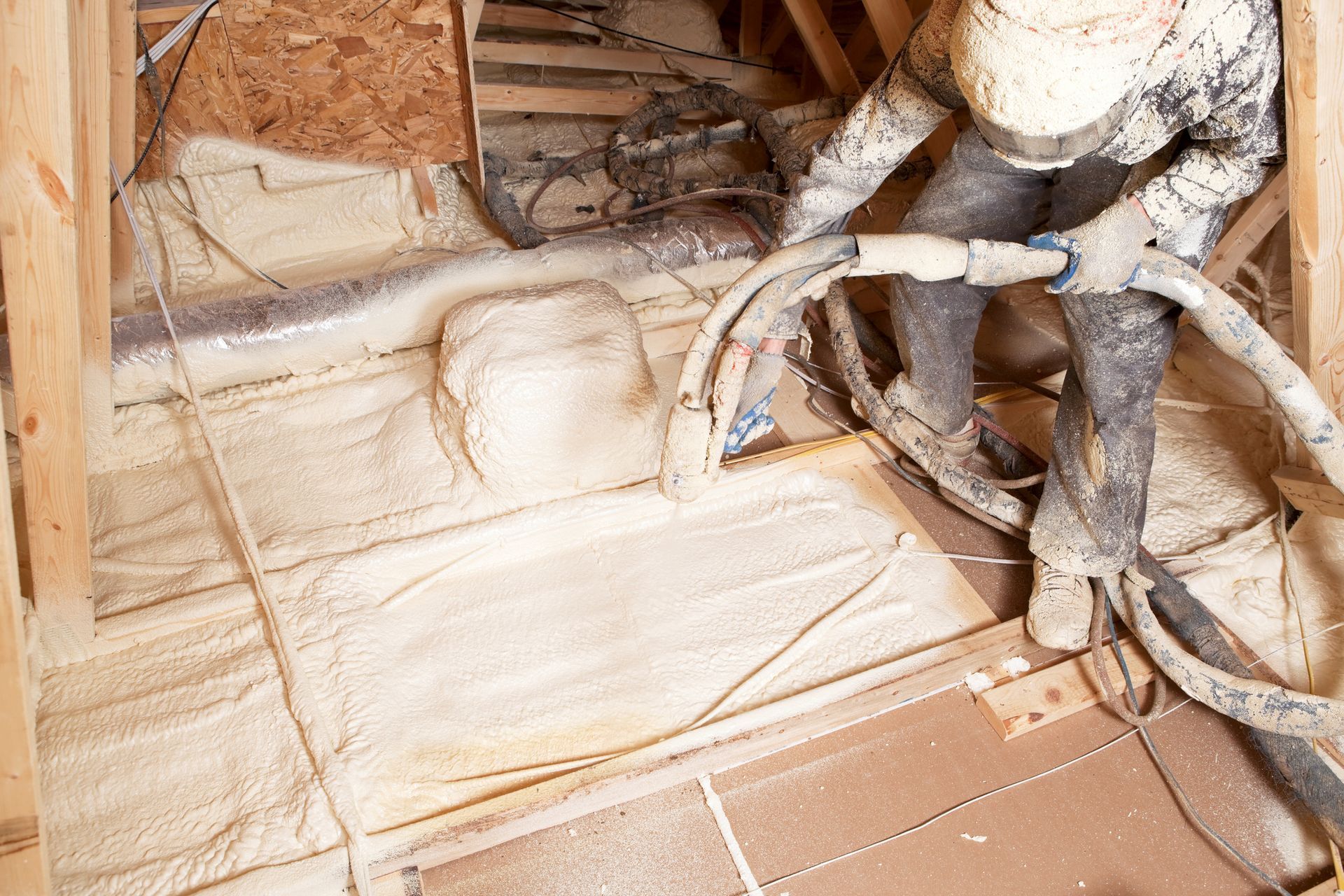 A man is spraying foam insulation on the floor of a house.