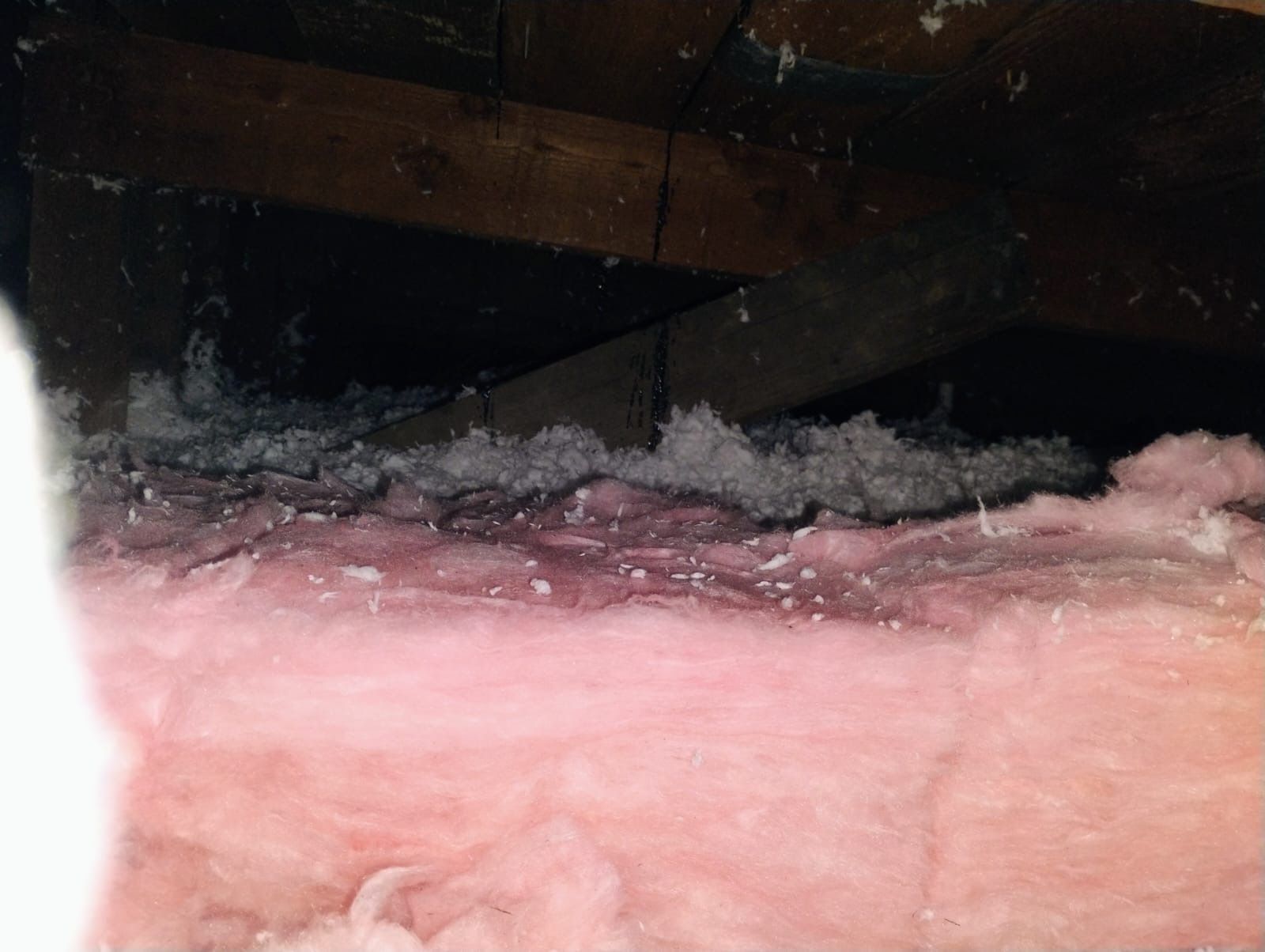 A close up of a piece of pink insulation in an attic.