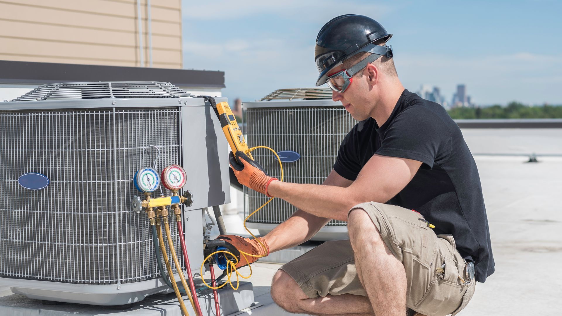 A man is working on an air conditioner on the roof of a building.