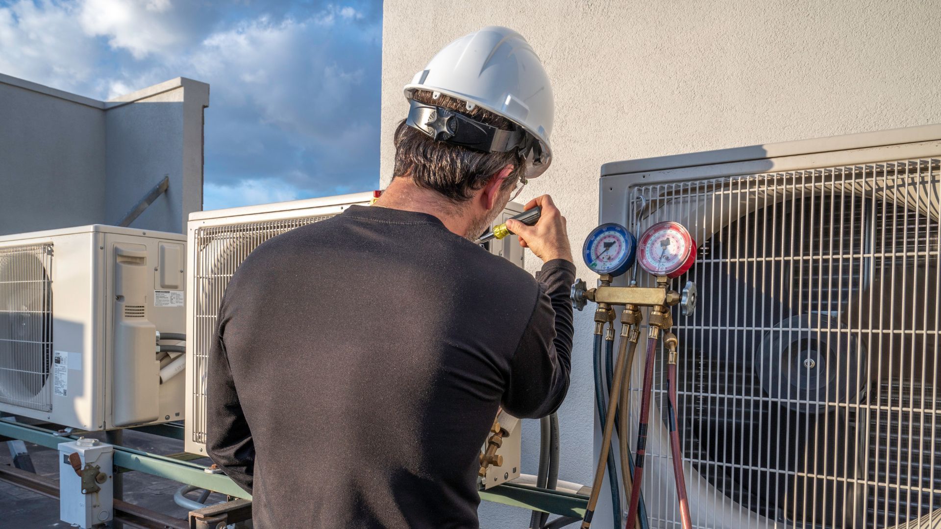 A man is working on an air conditioner on the roof of a building.