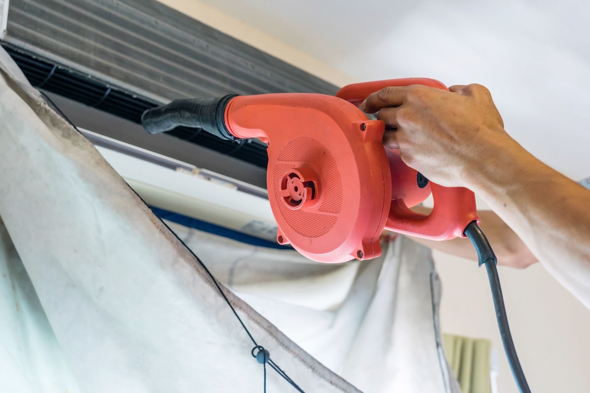 A person is cleaning an air conditioner with a blower.