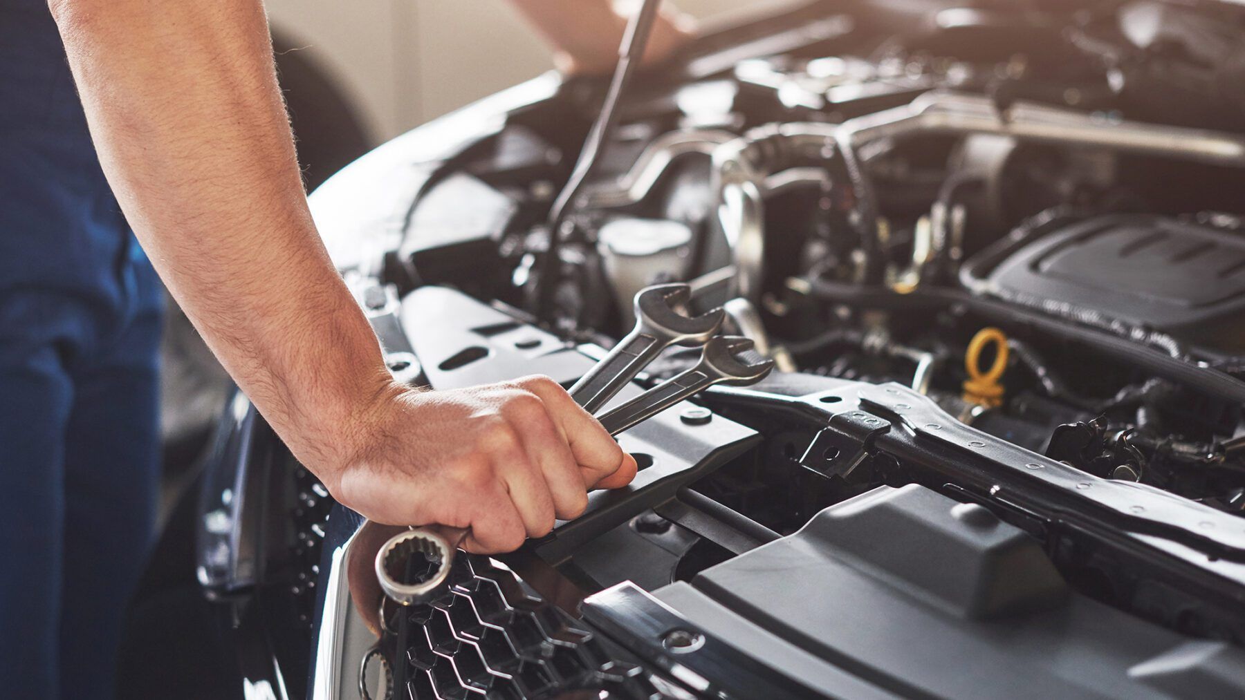 A man is working on the engine of a car with a wrench | Hopkins Tire & Auto Service