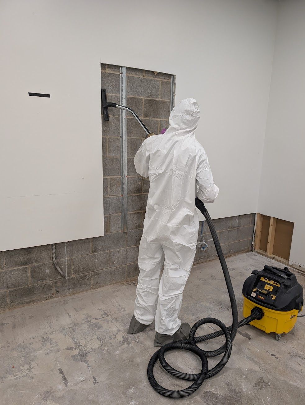 A man in a protective suit is cleaning a rug in a living room.